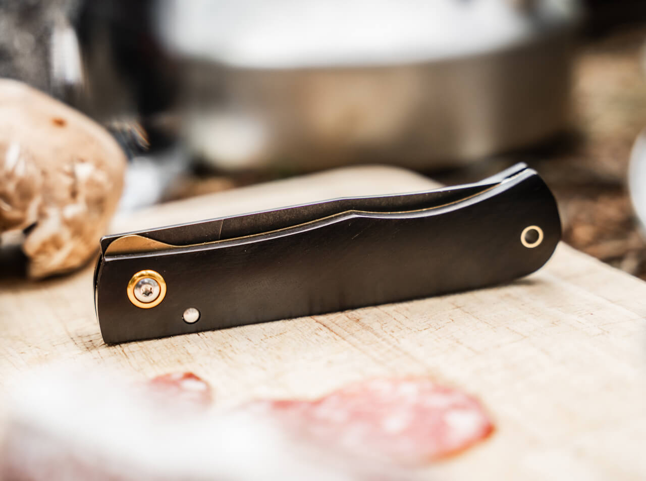 Black folding knife on a wooden surface with blurred background