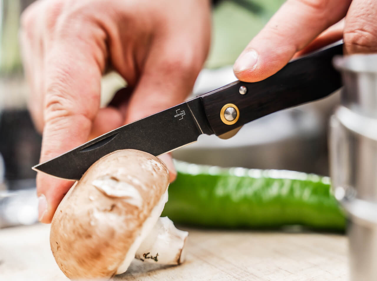 Person using a pocket knife to cut a mushroom on a cutting board with a blurred background
