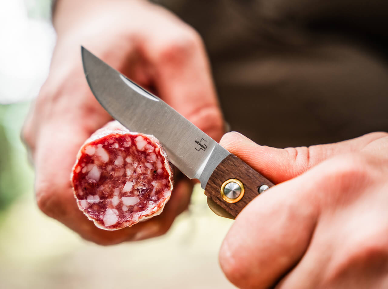 Person holding a knife cutting into a piece of cured meat.