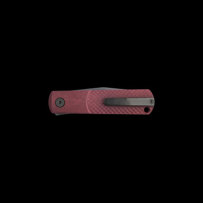 A folding pocket knife with a textured reddish-pink handle and a dark gray metal clip, shown horizontally against a solid black background.