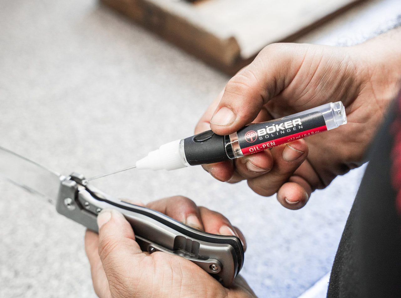 Person using a Boker oil pen on a pocket knife with a blurred background
