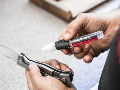 Person using a Boker oil pen on a pocket knife with a blurred background