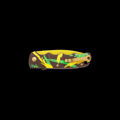 A folding pocket knife with a brown camouflage-style handle featuring yellow and green brushstroke patterns, a gold pocket clip, and a yellow inner scale, shown against a solid black background.