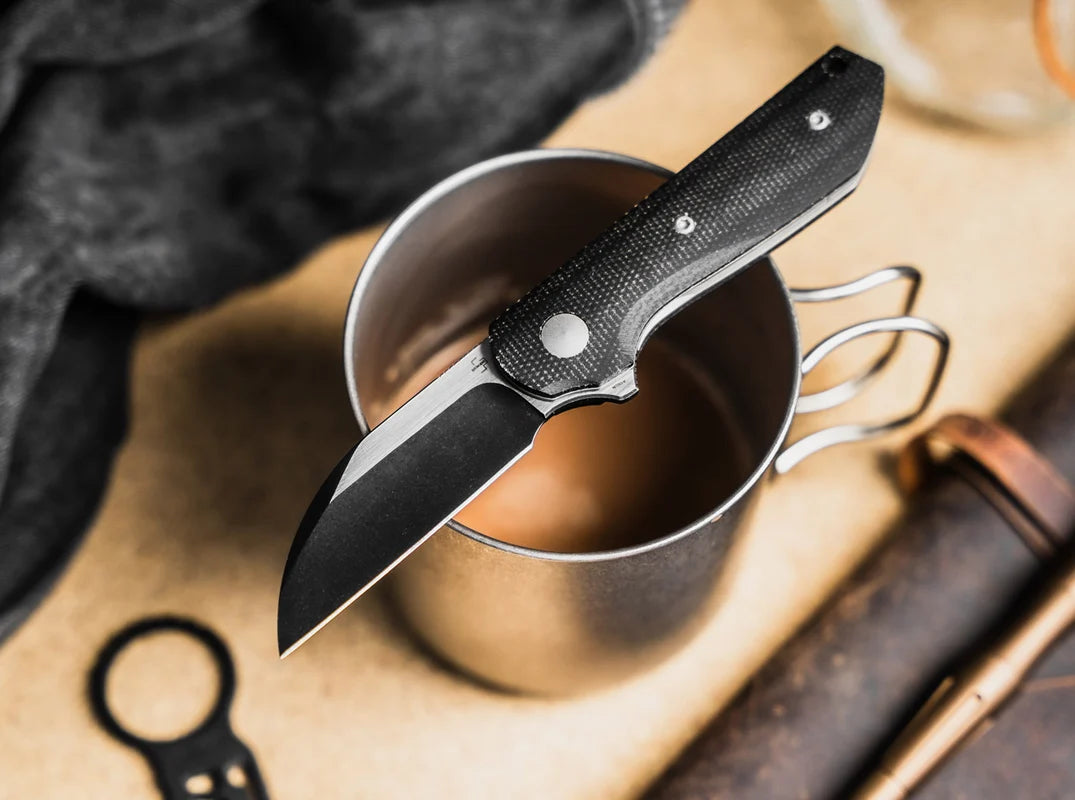 Folding knife on top of a metal cup with a blurred background