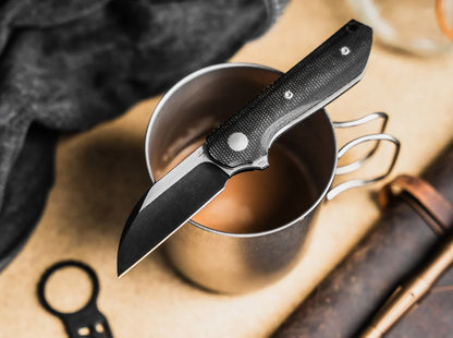 Folding knife on top of a metal cup with a blurred background